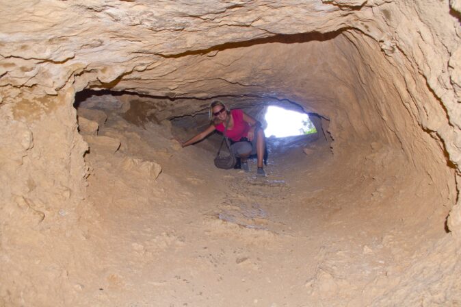 hiking on the Costa Blanca A woman smiling while climbing through a tunnel made of brown rocks