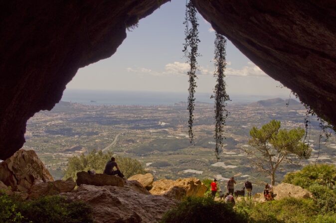 The Sierra de Bernia hike on the Costa Blanca panoramic view through rocks of a green landscape with the sea in the background and some hikers in the foreground