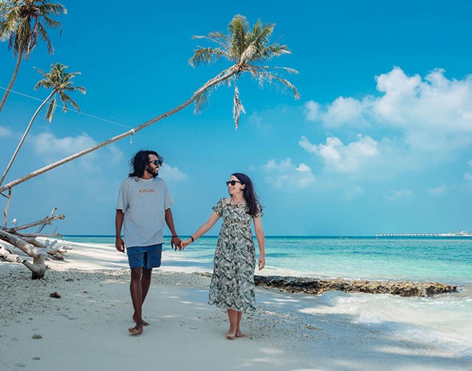 Dress code on local islands in the Maldives a couple holding hands, walking in a white sandy beach with palm trees