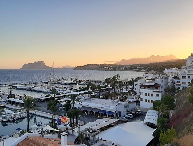 Sunset over a marina with the sea and mountains in the background