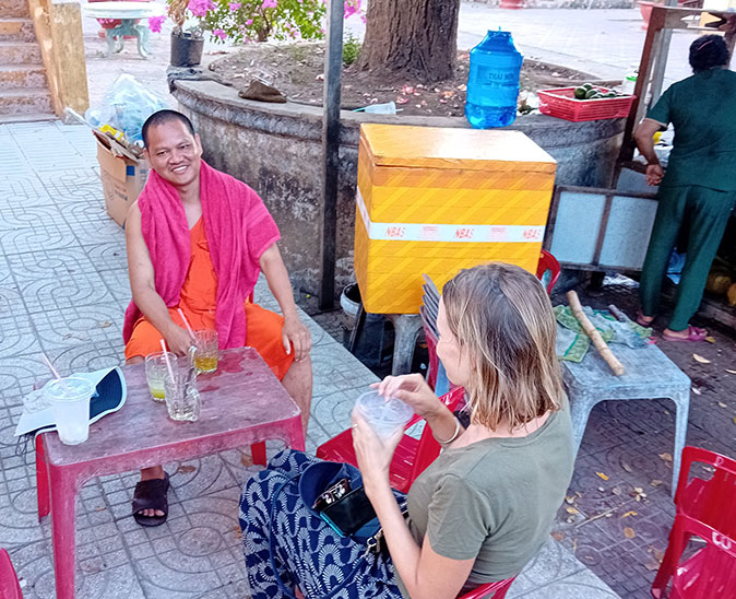 What makes someone a traveler? a woman facing a monk who is smiling, both sitting at a red table