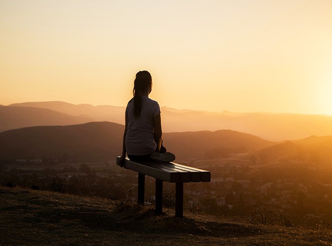 Is moving abroad right for you? A woman sitting on a bench on a hill looking at the view during sunset