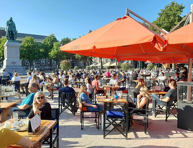 Visit The Hague A terrace filled with people and a bright orange umbrella