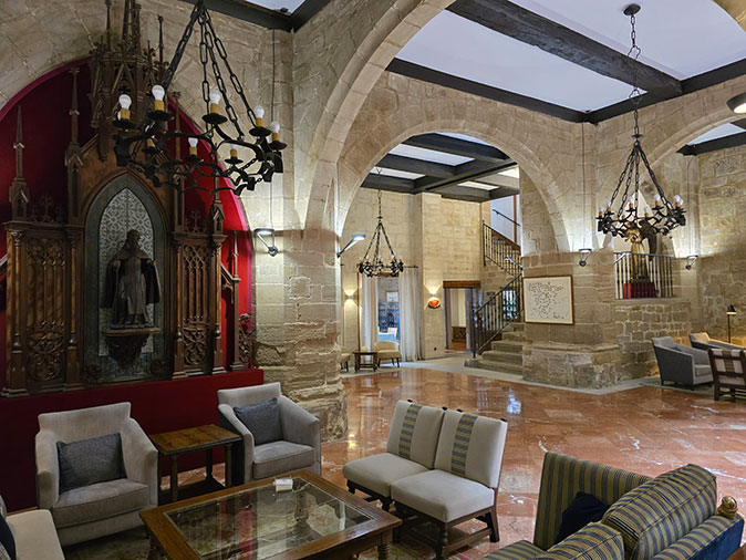 The lobby of one of the Paradores The lobby of a classic hotel with chairs, chandeliers and brown arches