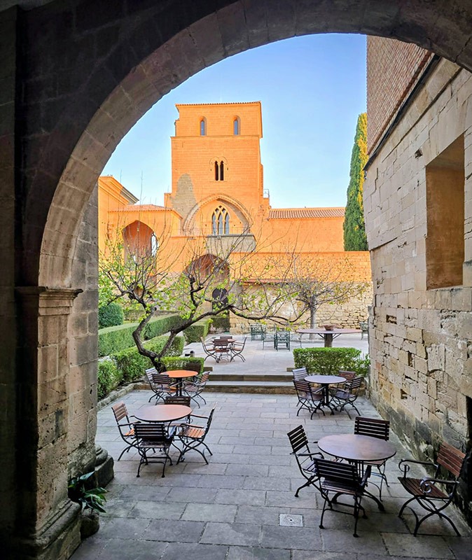A unique hotel experience in Spain Courtyard of a castle seen through an arch showing chairs and tables, part of the castle building and some greenery