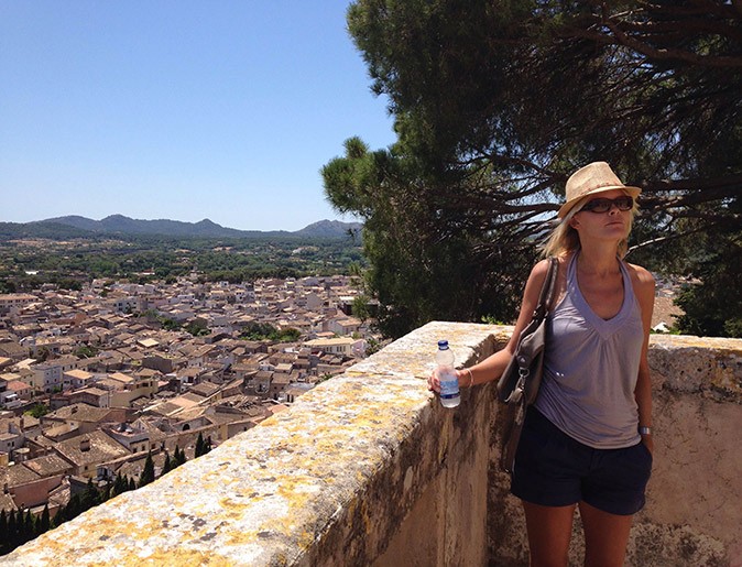 A woman with a hat and sunglasses, at a lookout point overlooking a Spanish town
