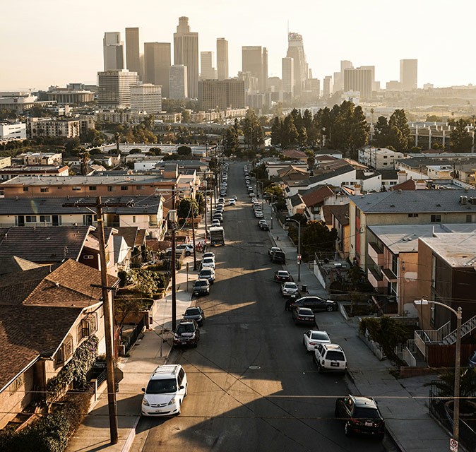 Los Angeles skyline An aerial view of Los Angeles showing high rise in the background and a row of villas in the foreground with cars parked on both sides of the street