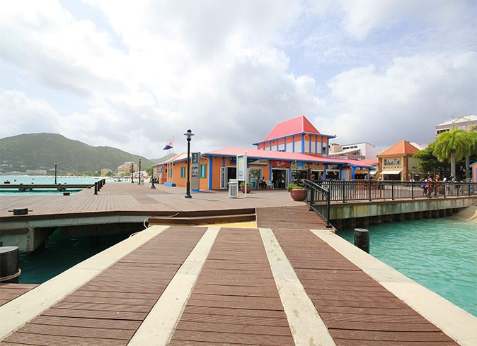 A wooden boardwalk with a pink and orange colored building plus bright blue sea in the background
