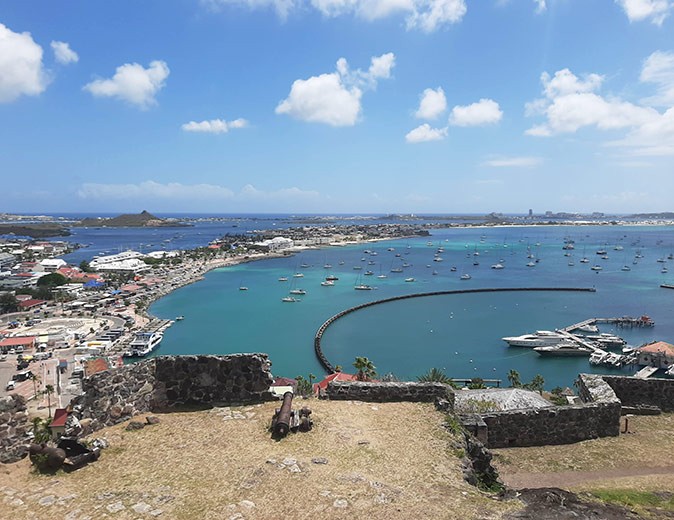 The top of a fortress with a view of a bright blue bay, several boats anchored and parts of islands