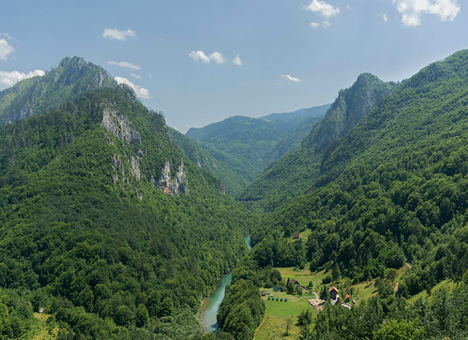 One of the reasons to visit Montenegro green mountains with a valley in the middle with a river running through it and a few houses