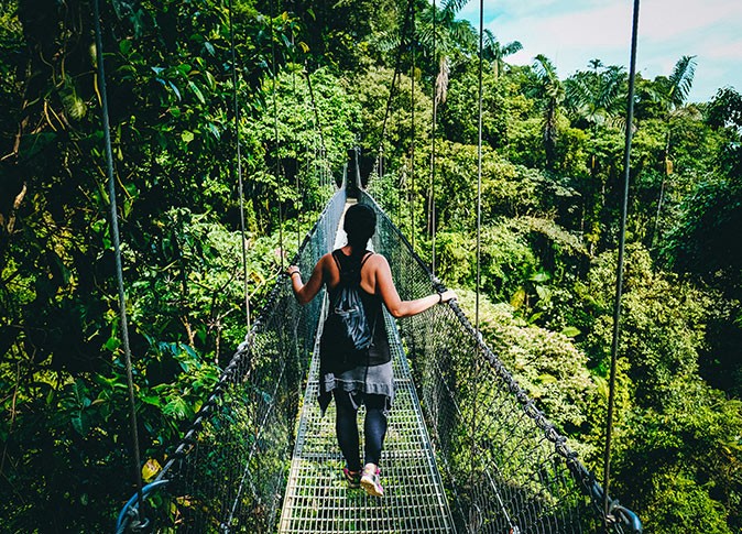 Enjoying life in Costa Rica A woman walking across a rope bridge surrounded by lush vegetation