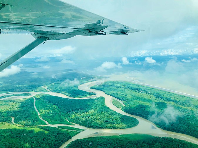 Flying over Costa Rica The wing of a small airplane with below it a green delta landscape and some clouds