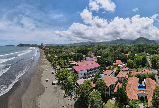 Living in Jaco, Costa Rica the ocean, a gray sandy beach, several buildings and a lot of greenery