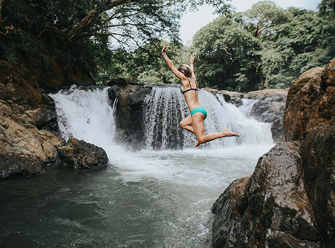 Living in Costa Rica as an expat A woman in a bikini jumping into the water in front of a waterfall surrounded by rocks