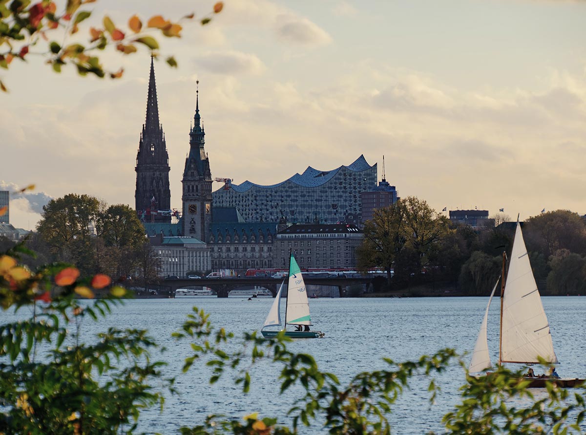 a lake with two sailboats with city buildings in the background