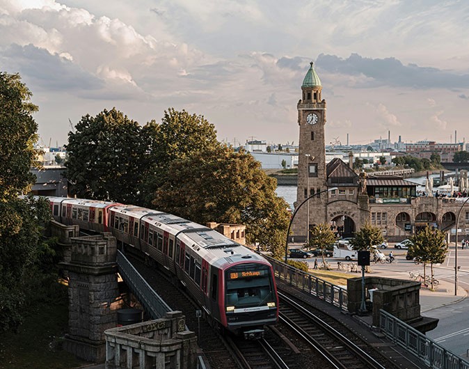 Is Hamburg a good place to live? a metro on an outdoor track with a street and city buildings in the background