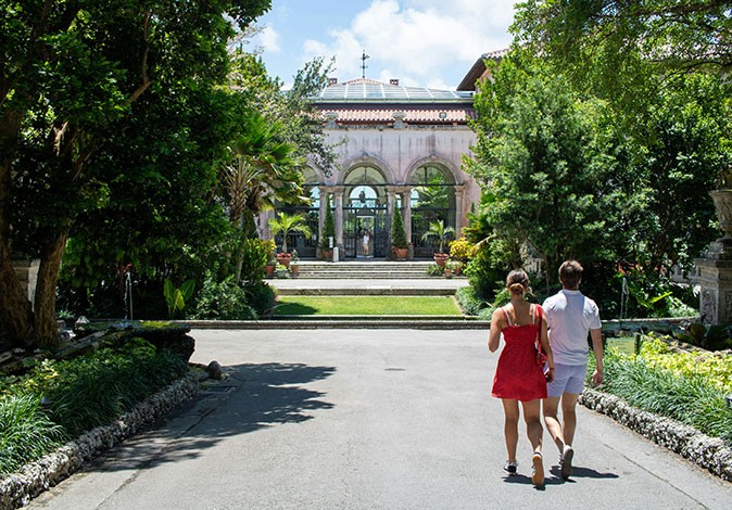 a man and a woman walking towards a historic building surrounded by greenery