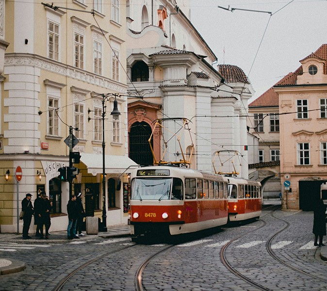 Life in Prague, Czechia A red and white tram in front of white and yellow buildings with several people on the sidewalk