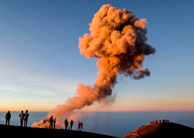 hikers at the top of Acatenango volcano, looking at smoke coning out of Fuego volcano