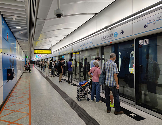 Pros and cons of living in Hong Kong People waiting to board a metro in a modern, mainly gray metro station