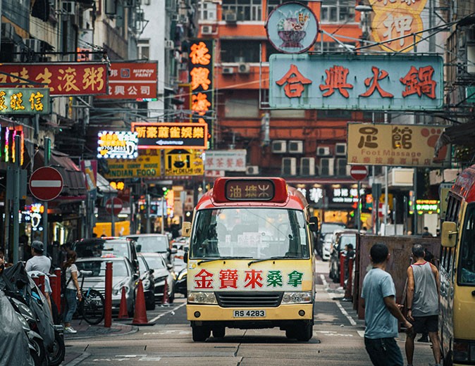 Safety in Hong Kong as a place to live A red and yellow bus with Chinese writing on a street with many large signs with Chinese writing