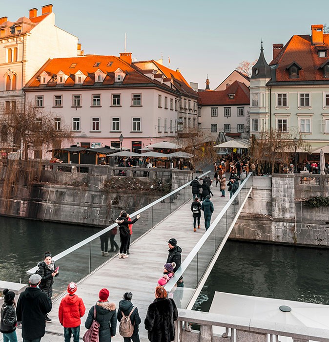One of the least visited capital cities in Europe Several people walking across a modern bridge with historic city buildings in the background