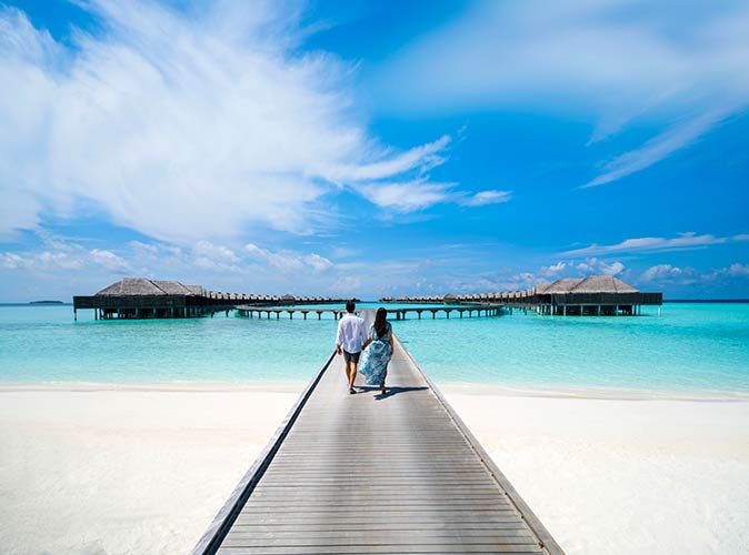 a couple walking on the dock towards the over water villas in Kihavah Maldives resort