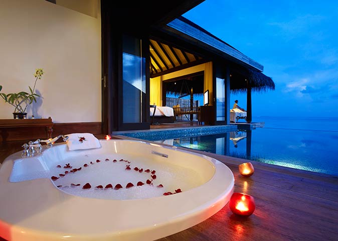 rose petals in the shape of a heart in the bathtub of an over water villa in the Maldives at sunset