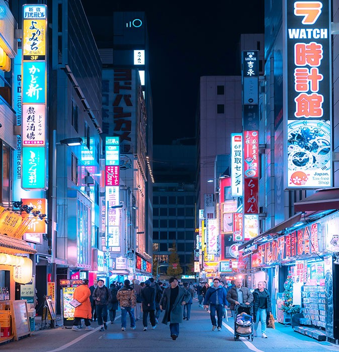 Tokyo, a safe city to live in a pedestrianized street with people walking after dark, surrounded by highrise buildings and many neon signs