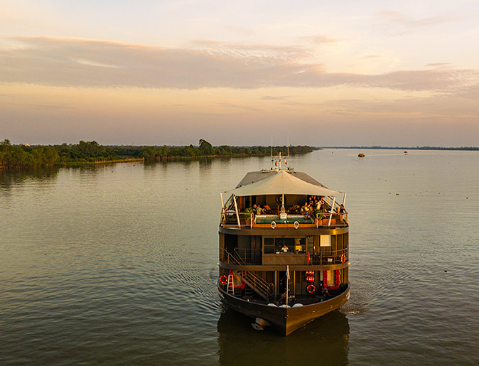 Going on a cruise to discover new destinations A small cruise ship at sunset showing calm water and a shoreline with lush greenery