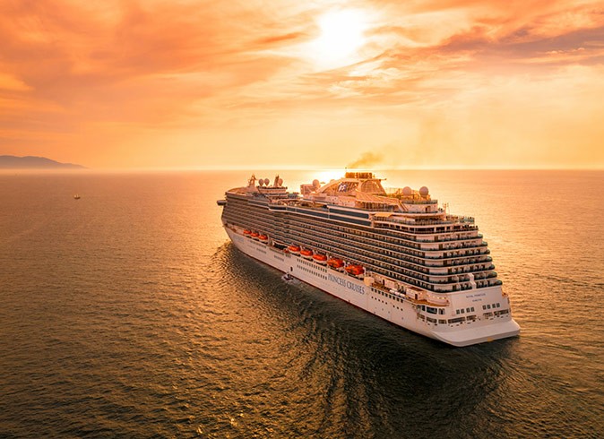 Why you should go on a cruise A large cruise ship surrounded by water, in warm orange light from the setting sun