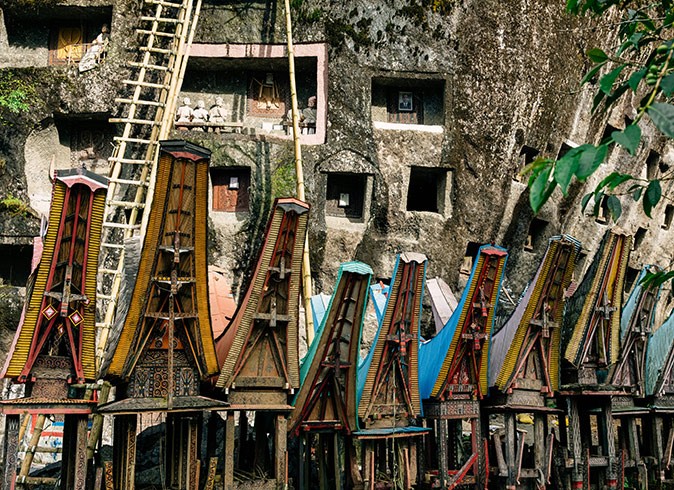 A row of wooden structures in front of a stone cliff that all forms part of special burial grounds