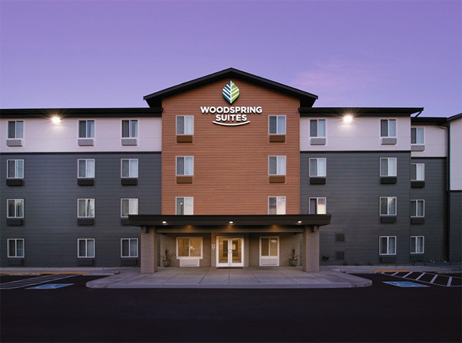 The exterior of a hotel building with white, gray and brown parts, with part of an empty parking lot in front of it