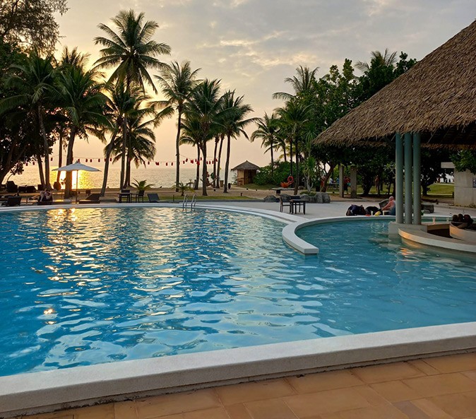 Tips for staying in a hotel A large swimming pool with the beach, palm trees and sunset in the background