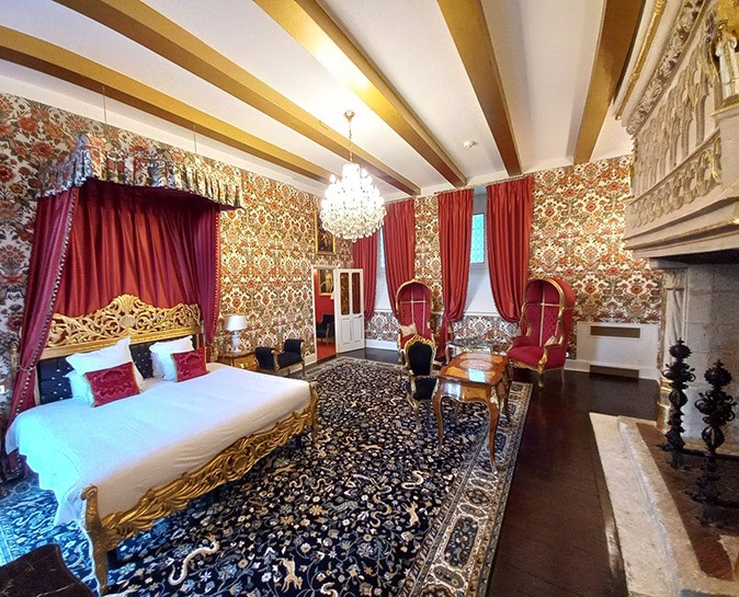 A unique hotel room in France - I often look for more unique hotels A large hotel room decorated like a palace with red curtains, gold touches throughout and a large bed