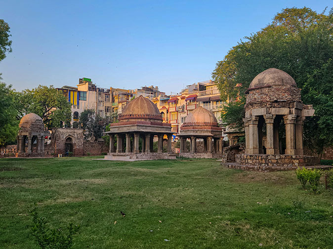 Remains of ancient stone structures with a park in the foreground and grey city buildings in the background