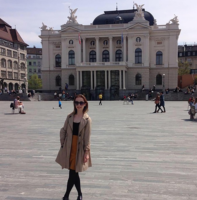 An expat living in Zurich A woman with brown hair and sunglasses standing on a city square in front of a historic white and gray building