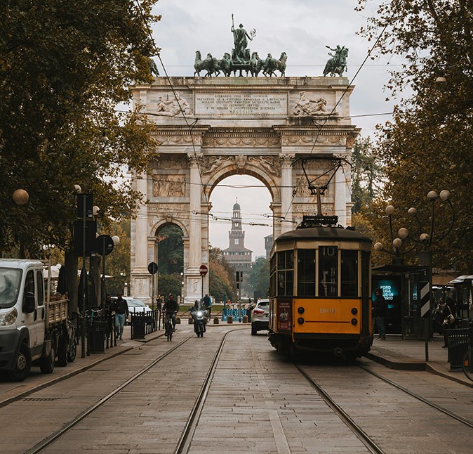 An orange and brown tram in front of a historic city arch