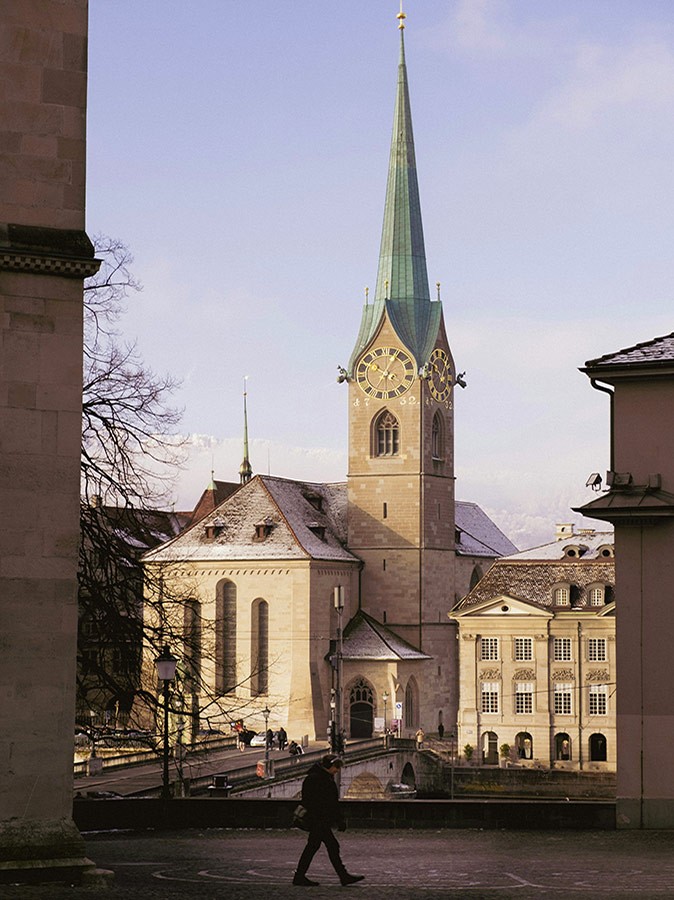 Zurich travel guide: one of the main things to do A beige church with a green roof and a stone bridge in front of it with some people