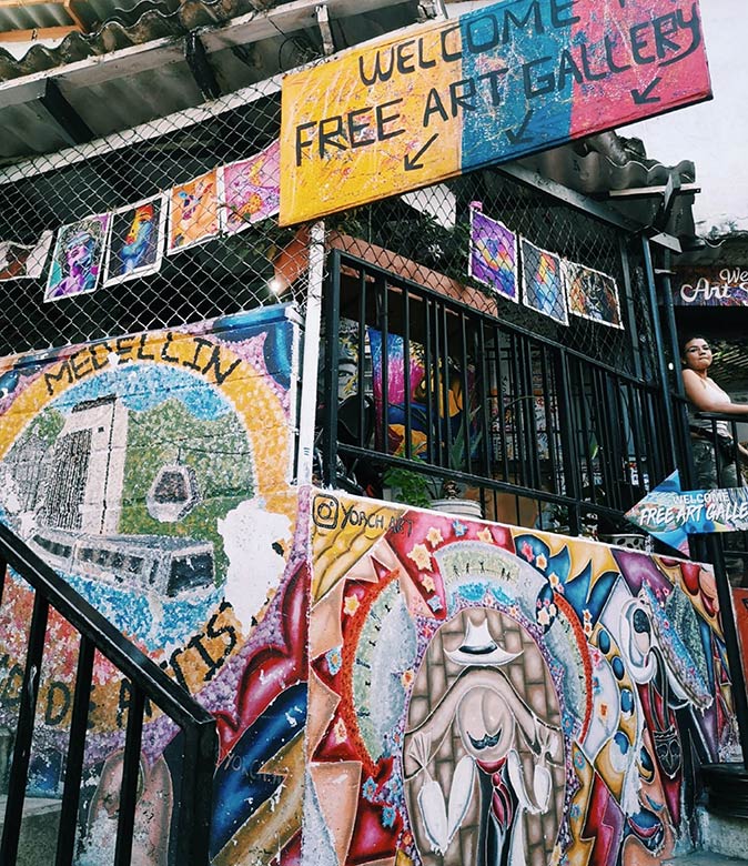 Life in Medellin colorful paintings with a sign saying 'welcome - free art gallery'