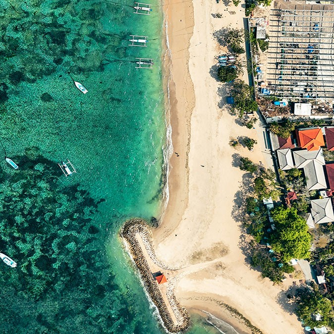 Digital nomad life in Sanur, Bali Aerial view of a coastline with fishing boats anchored, white sandy beach and some houses