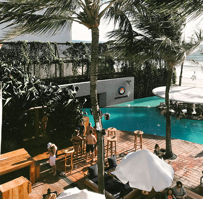 Digital nomads in Seminyak, Bali A terrace with several people, wooden tables, white umbrellas, palm trees and a swimming pool