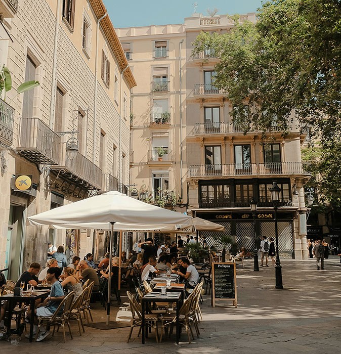 Life in Barcelona A terrace on a city square, filled with people, with white umbrellas, surrounded by apartment buildings