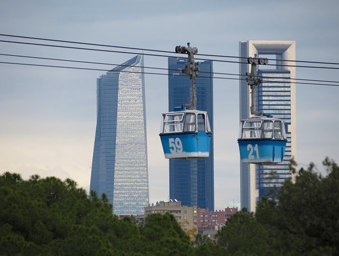 One of my favorite things to do in Madrid 2 blue and white cable cars with skyscrapers and some greenery in the background