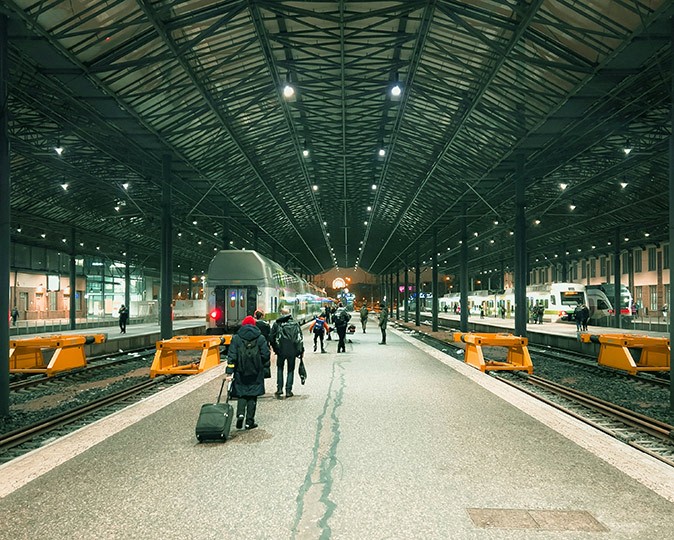 A modern looking train station showing several trains and people with luggage walking towards the trains
