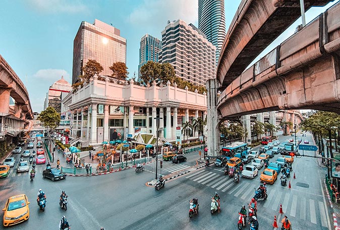 a busy road crossing with cars and motorbikes, surrounded by highrise