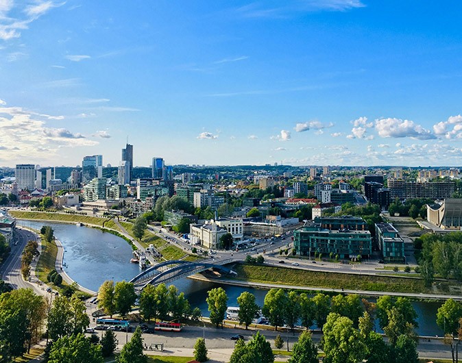 One of the best places to visit in Lithuania Aerial view of a city with modern buildings by a river, with a blue sky