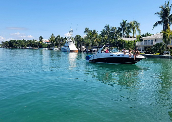 Boating in Miami, Florida Several people sitting on the bow of a motorboat as it cruises past a coastline with houses and palmtrees