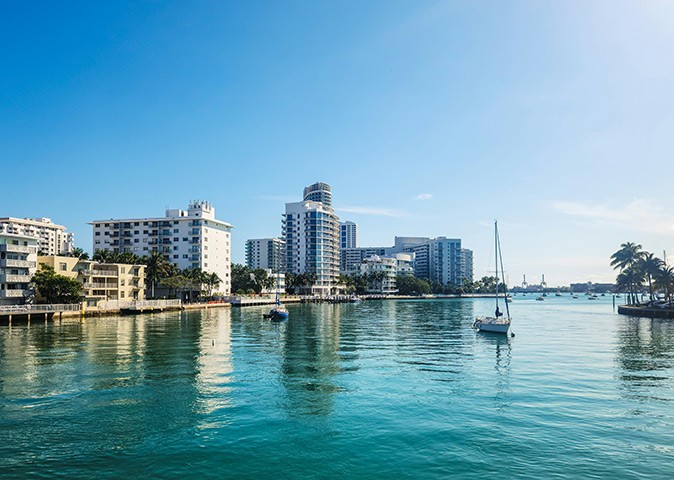 One of the best boating spots in Miami Several boats anchored in a bay with turquoise water, showing modern highrise buildings on shore