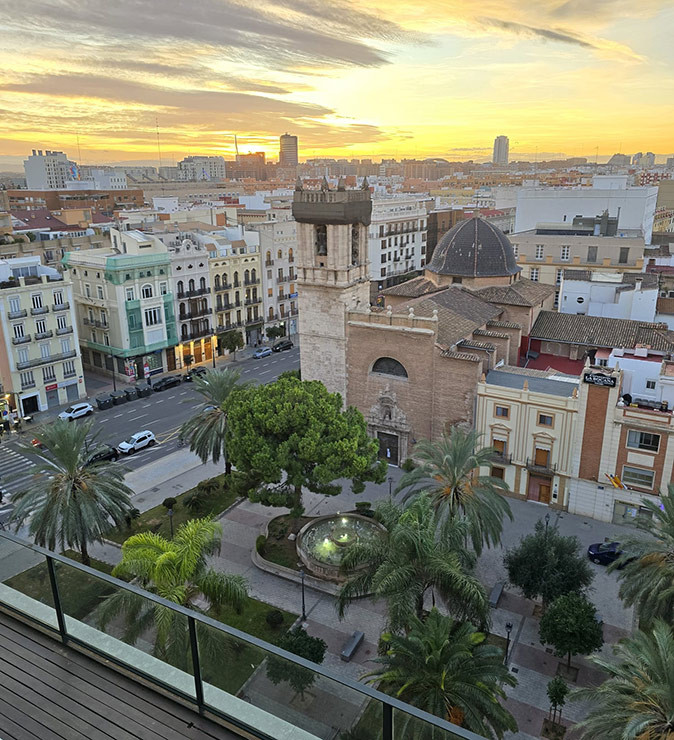 Aerial view of a neighborhood in Valencia showing a historic church, several apartment buildings, cars and a plaza with trees and a fountain